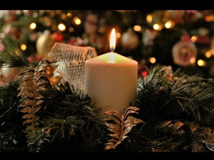 Candle glowing on a Christmas wreath with soft lights in the background